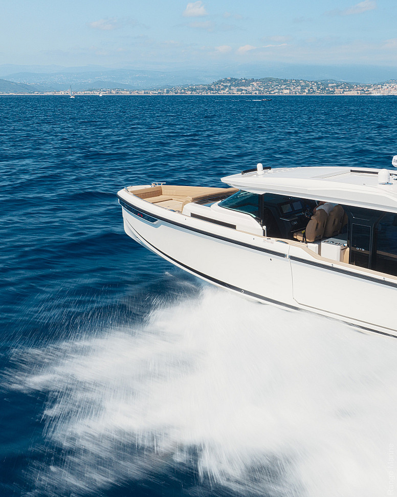 Saxdor 460 GTS на ходу, вид с борта: белый корпус, пенный бурун у борта, вдали береговая линия